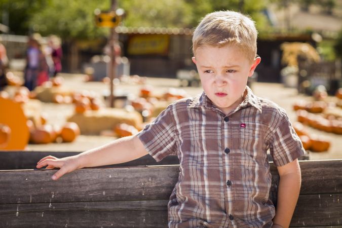 Adorable Little Boy Standing Against Old Wood Wagon at Pumpkin Patch in Rural Setting