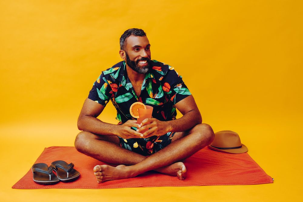 Black male sitting on towel and looking to his side while holding tropical drink