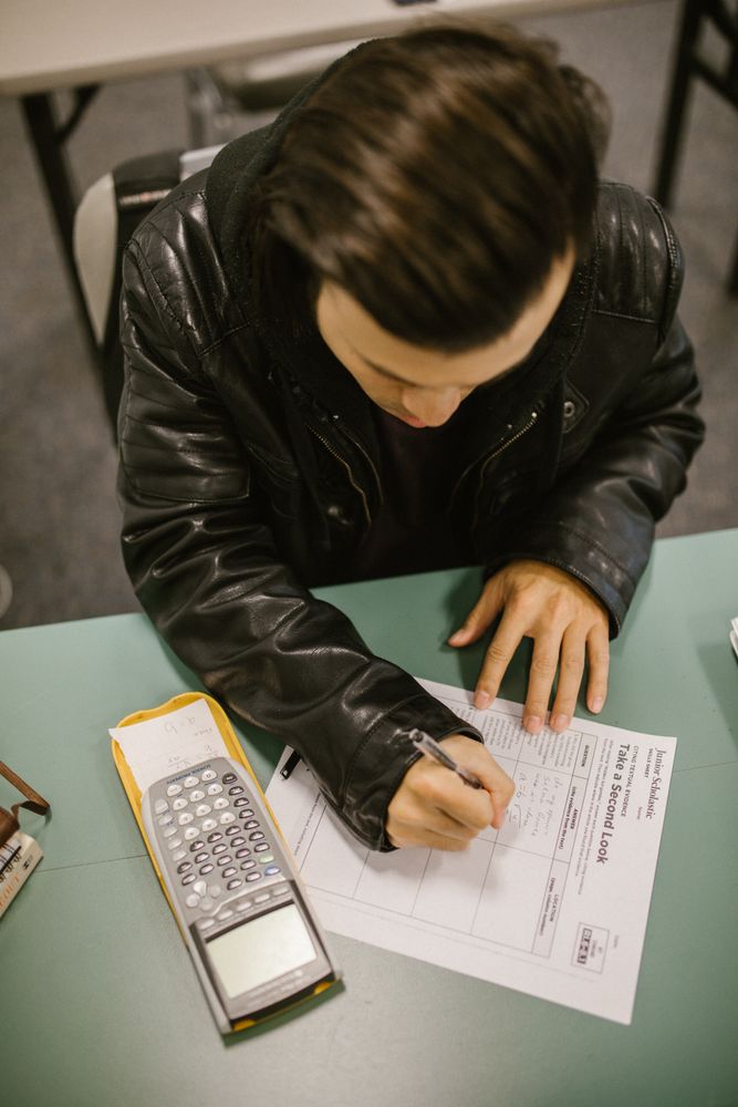 Top view of young man writing on a paper and sitting at a desk in classroom