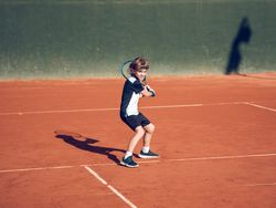 Athletic kid with racket playing tennis on clay court