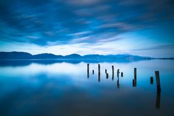 Wooden pier or jetty remains on a blue lake at sunset, Versilia, Tuscany, Italy
