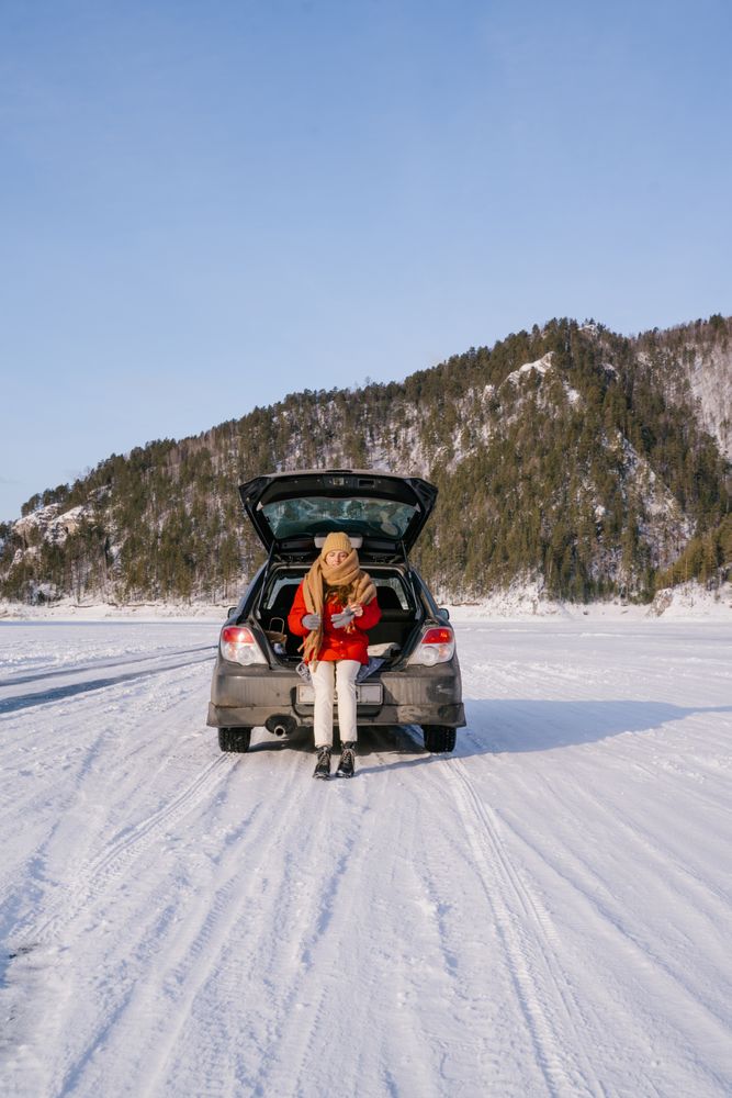 Woman sitting on car trunk in snowy valley