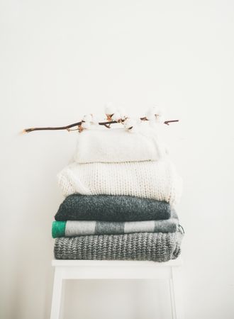 Pile of clean, folded sweaters on light background with dried cotton, copy space