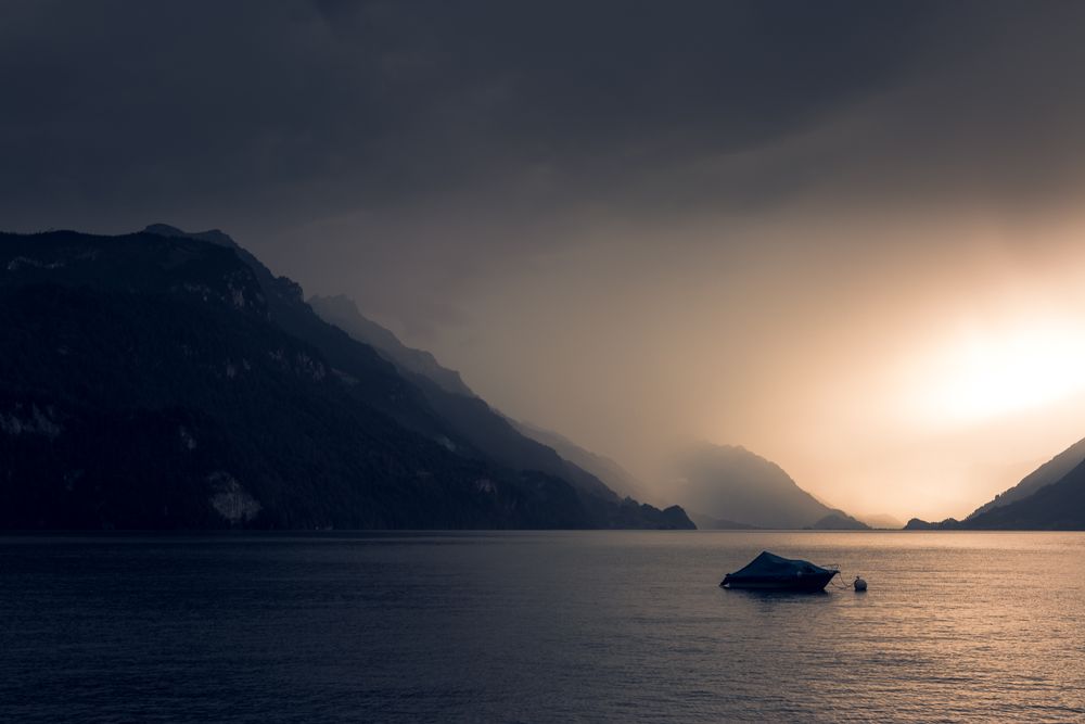 Lonely yacht in gray water with dark mountains under cloudy sky