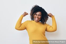 Happy Black woman flexing her arms muscles in a yellow turtleneck 0y2kW5