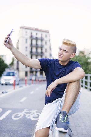 Young blonde man sitting outside and taking a selfie