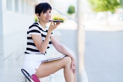 Woman talking on speaker phone as laptop rests on her legs
