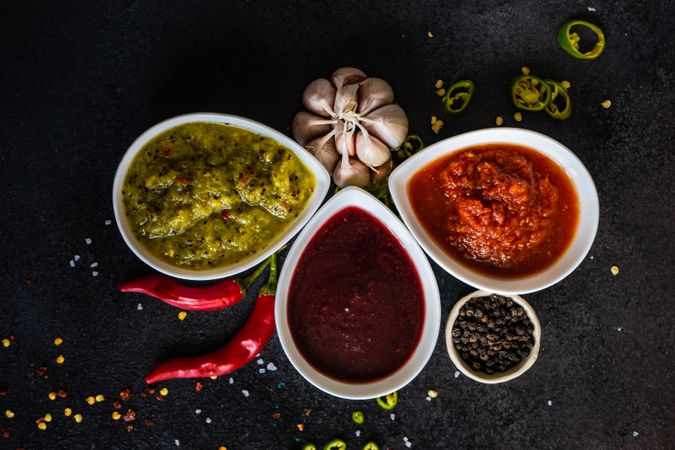 Top view of flavorful spicy traditional Georgian sauces on dark counter with garlic and chilis