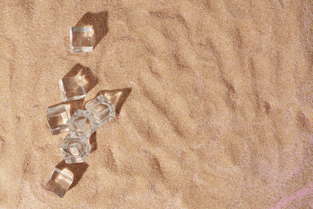 Flat lay of ice cubes on sand with shadow