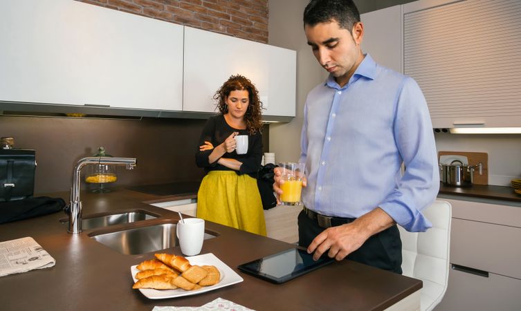 Tense couple looking at news on tablet while having quick coffee in home before work