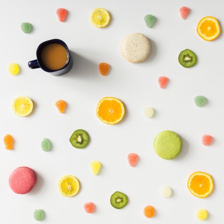 Fruit slices, gummies, and macarons and coffee cup on light background