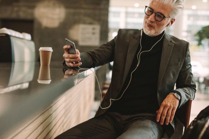 Mature businessman texting on smart phone while listening to music on earphones at cafe