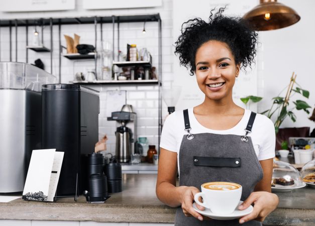 Smiling barista holding a large cappuccino in front of machines