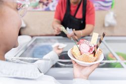 A young Hispanic woman is waiting for her change while holding a big traditional Mexican ice cream