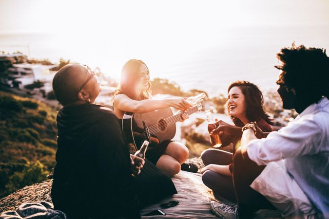 Group of friends laughing outside with drinks and guitar