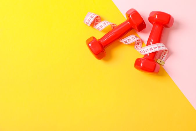 Dumbbells and measuring tape on two tone background, copy space