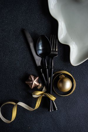 Dark cutlery on dark background tied with festive gold ribbon, and baubles
