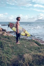 Athletic barefooted man with surfboard admiring sea on grassy sh