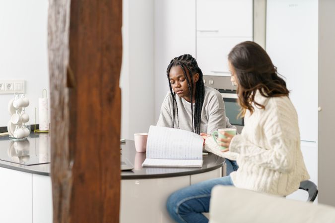 Two serious women sitting at kitchen table and working on something on a laptop