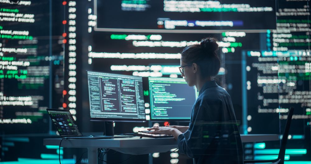 Female Developer Thinking and Typing on Computer, Surrounded by Big Screens Showing Coding Language.