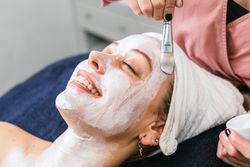 Anonymous professional beautician applying facial mask on face of client