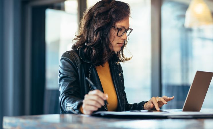 Woman entrepreneur sitting at the table writing notes while working on laptop