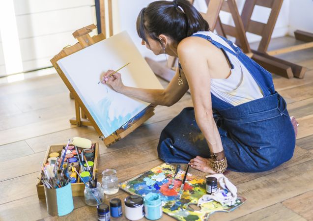 Woman artist painting on a canvas a blue abstract painting. Creative ywoman working on the floor in her art studio.