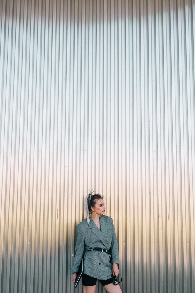 Woman with tablet in stylish suit standing nearby wall holding sunglasses