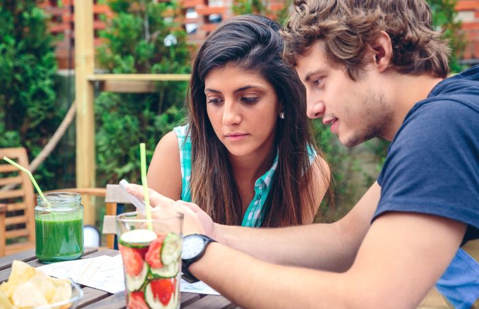 Male showing female friend something on phone at outside table