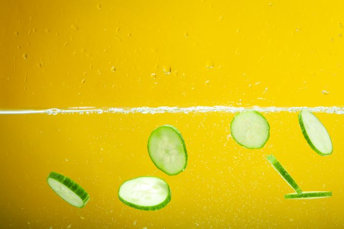 Cucumber slices floating in water in yellow background
