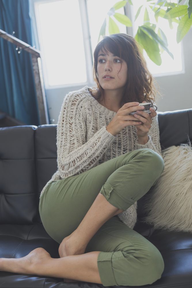 Female on cozy sofa with cup of tea, vertical