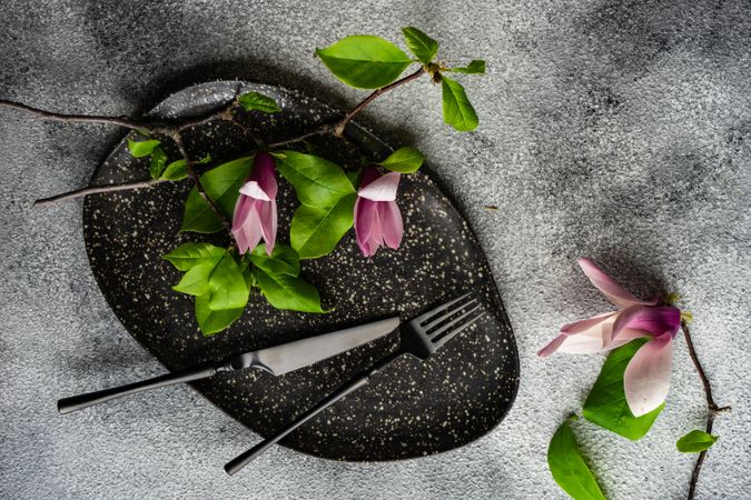 Top view of dark plate with magnolia flowers on grey table