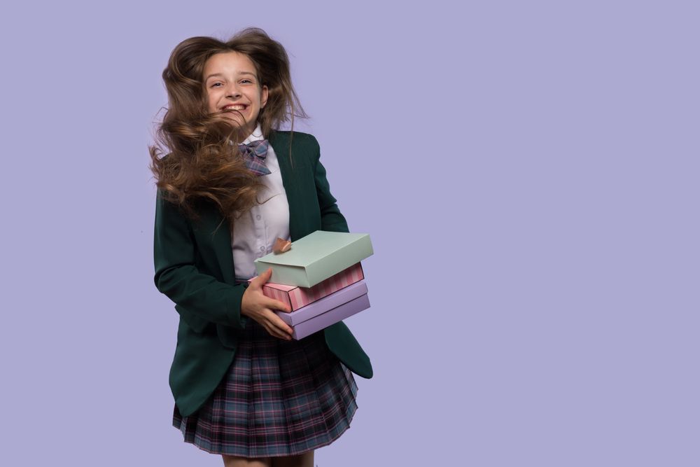 Schoolgirl holds colorful gift boxes with hair blowing in wind.