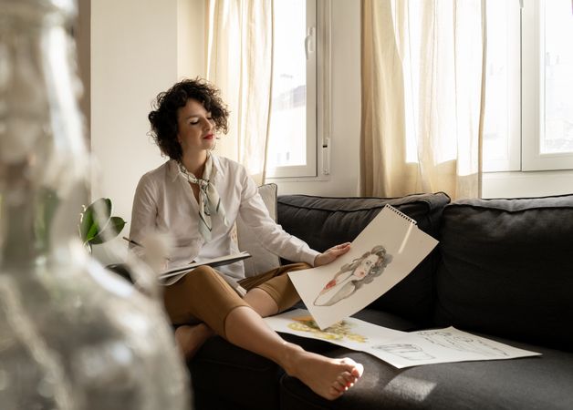 Woman drawing on papers on sofa in room