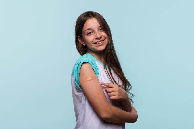 Girl smiles while pointing to bandage on arm