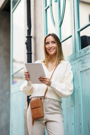 Smiling woman in cream standing outside with digital tablet