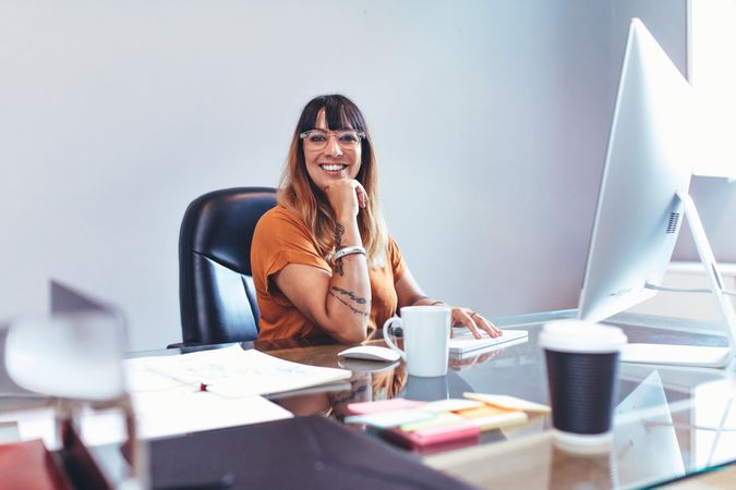 Smiling businesswoman sitting at her desk in office with hand to her chin