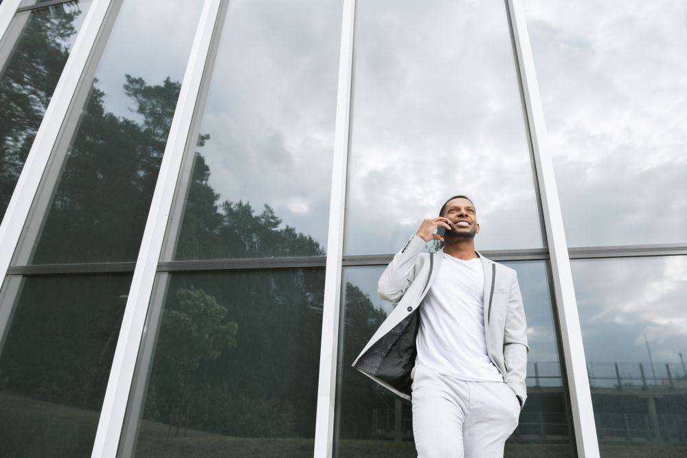 Elegant Black man talking smartphone leaning building