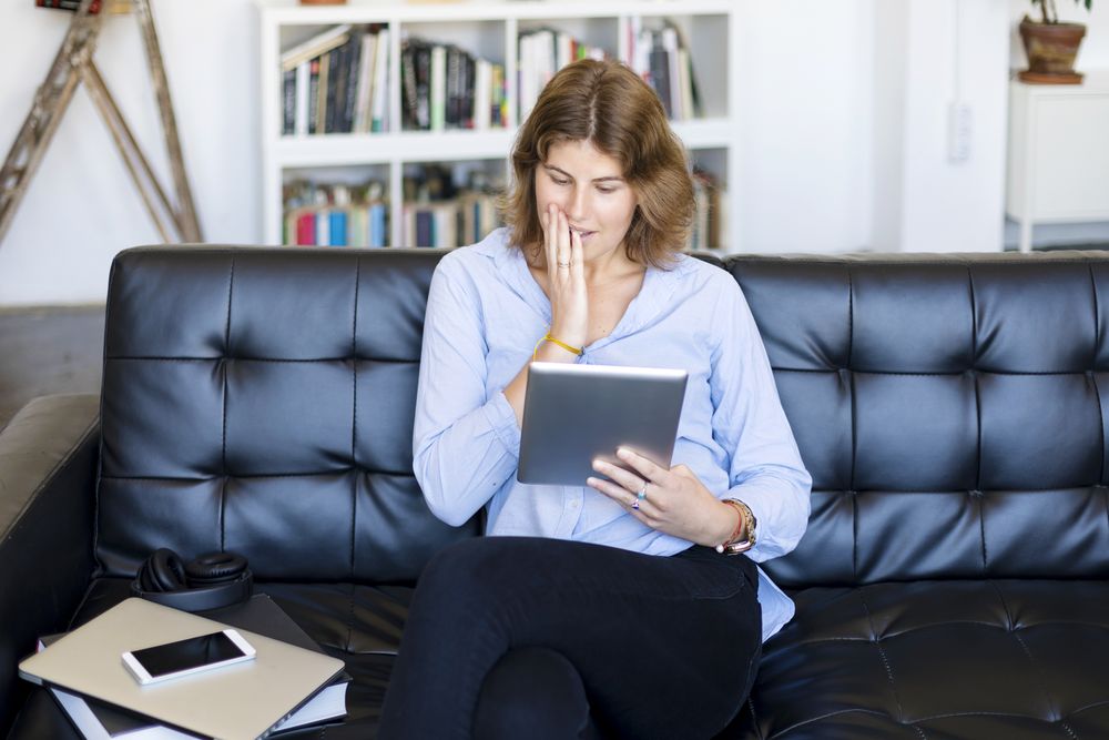 Female sitting on couch at home and surprised by something on a digital tablet