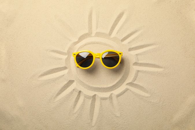 Painted sun and yellow sunglasses on sea sand