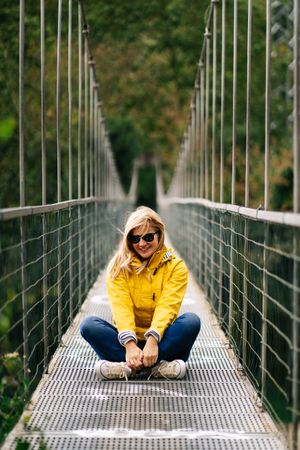 Cheerful female tourist standing on hanging bridge in summer
