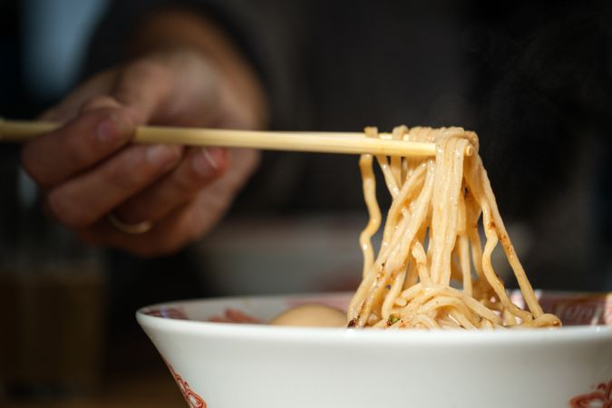 Crop person eating ramen with chopsticks