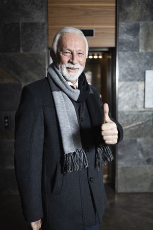 Man in suit and scarf giving thumbs up outside elevator