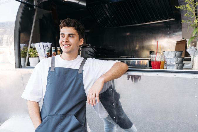 Content male in apron leaning in window of food truck