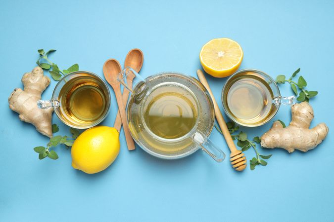 Cups and teapot with tea, lemon, ginger on blue background, top view