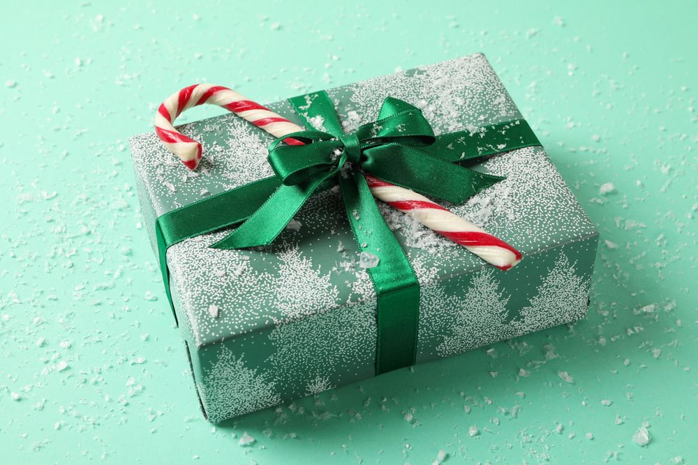 Christmas box with candy cane on mint background with snow