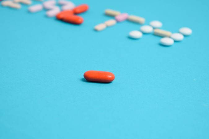 One pill in front of others spelling the word "HEALTH" on blue table