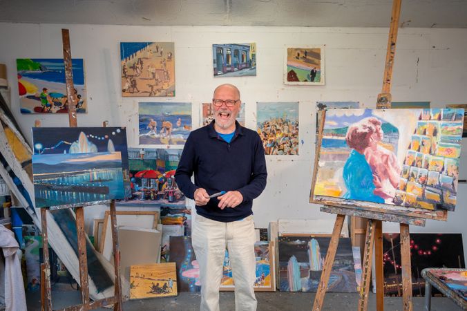 Smiling older male surrounded by paintings in art studio