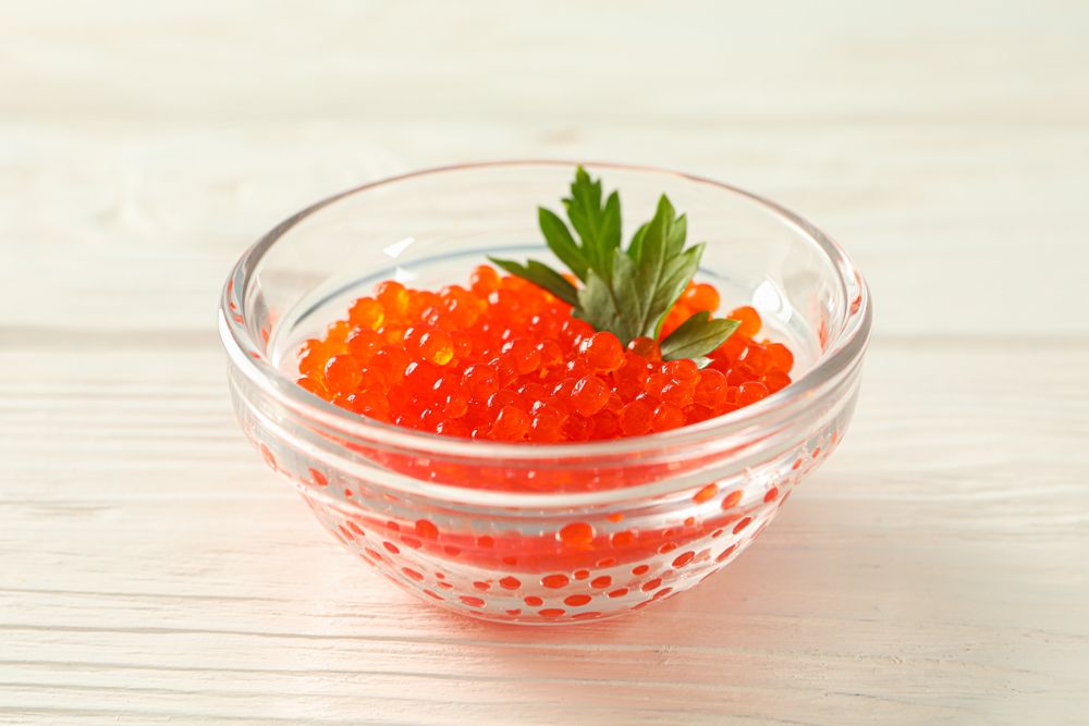 Glass jar with red caviar isolated on wooden table, space for text