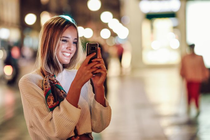 Chic smiling woman with scarf in hair taking photo with phone with copy space